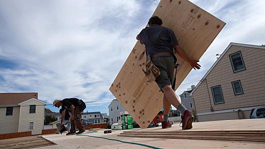 Emile Wamsteker | Bloomberg | Getty Images  A construction worker carries a sheet of plywood as he and co-workers install the sub-floor of a home onto pilings. 