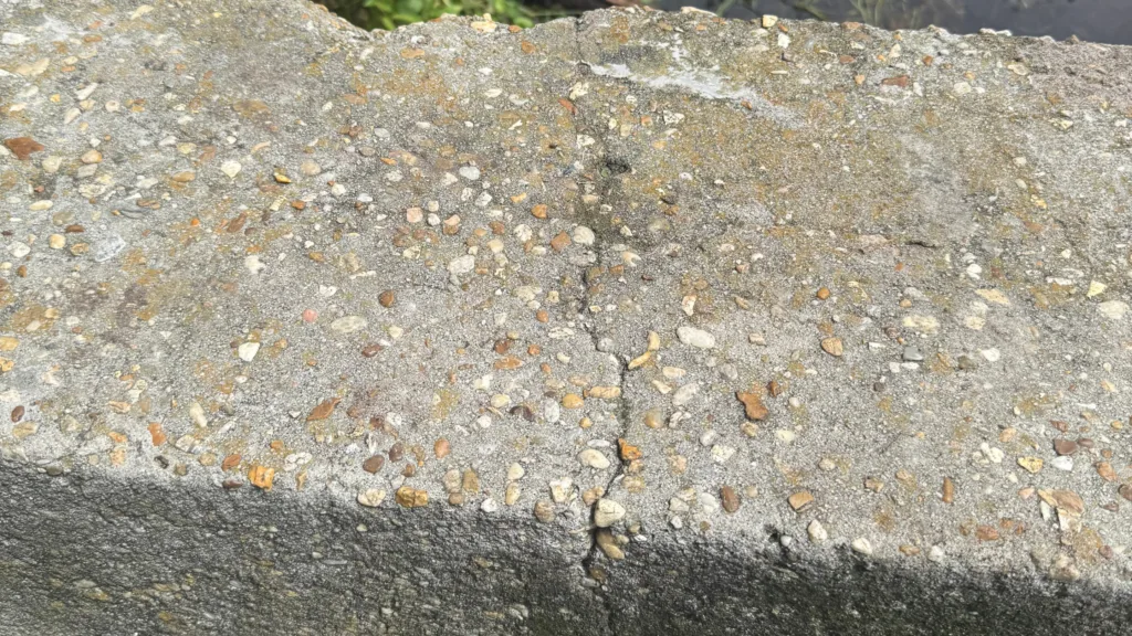 Close-up of structural cracks and exposed aggregate in aging concrete spillway at Lake Lulu dam, requiring stabilization.