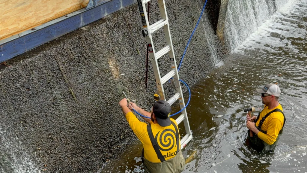 Helicon crew injecting polyurethane foam into dam wall to stabilize soil and fill voids beneath spillway structure.