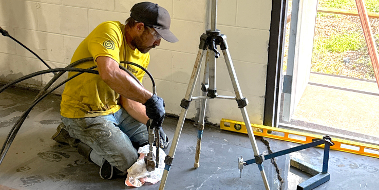 Foreman injecting polyurethane grout under a concrete slab in a commercial building.