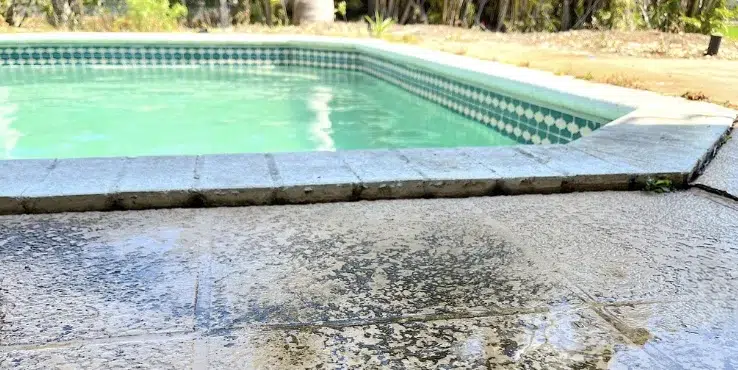 Close view of an unlevel pool deck showing worn concrete and water damage along the edge of a residential swimming pool.