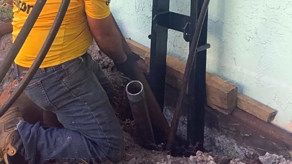 Technician installing a steel foundation pier beside an exposed home footing during foundation repair.