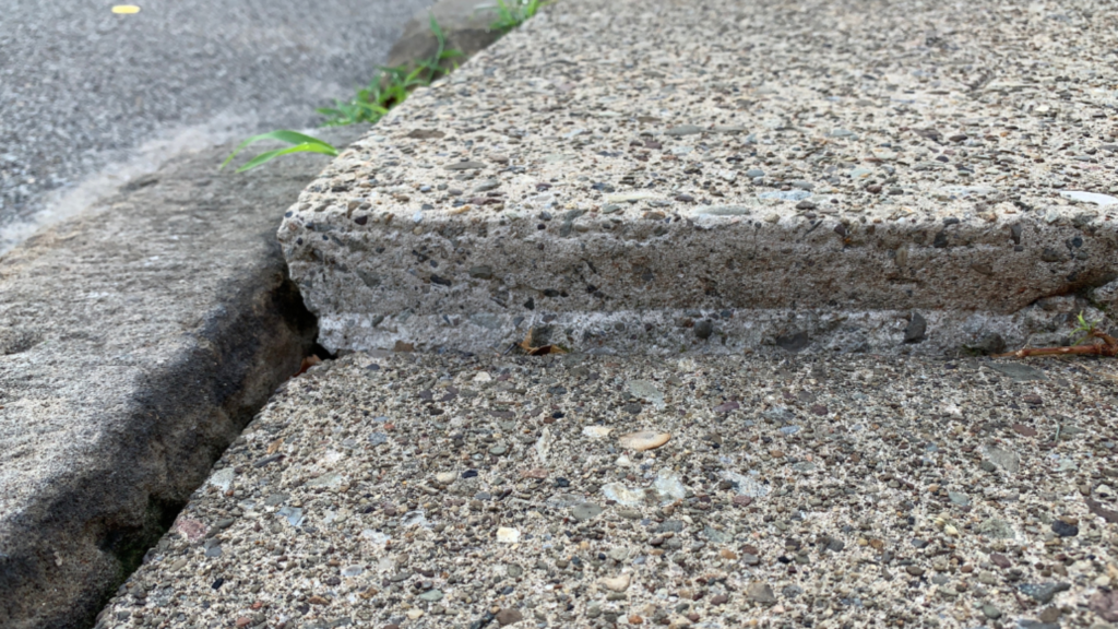 Sunken residential concrete slab with visible separation and uneven settling caused by soil erosion
