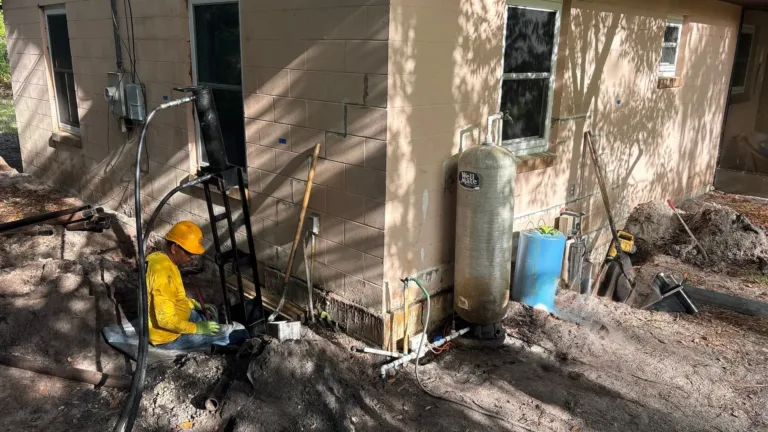 Foundation repair work in progress with a technician operating hydraulic equipment beside an excavated wall.