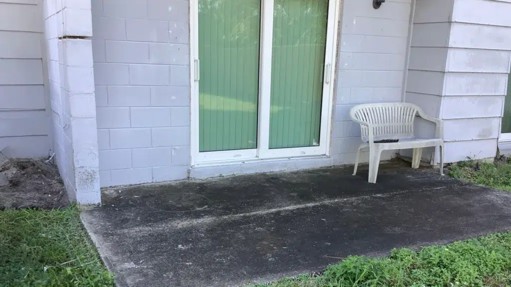 Exterior view of a residential concrete block foundation wall surrounding a sliding glass door, showing slab surface conditions and adjacent wall areas inspected during a foundation movement evaluation.