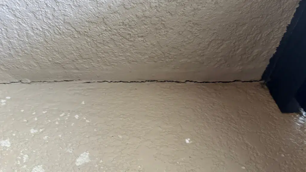 Separation crack visible where stucco ceiling meets exterior wall due to settlement